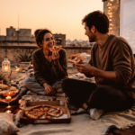 A vibrant, high-quality image depicting a couple engaged in an unusual and fun activity outdoors, like stargazing on a rooftop, painting together in a quirky studio, or having a picnic in an unexpected urban spot. The atmosphere should be joyful, intimate, and full of connection, emphasizing shared laughter and unique experiences. Use warm, inviting colors and soft lighting. Focus on their interaction and the unique setting, not just the faces. Artistic, cinematic style.